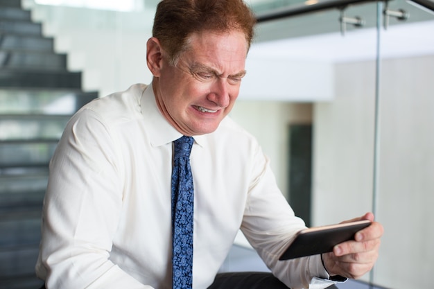 Angry senior businessman reading message on phone