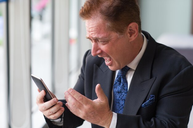 Angry senior businessman shouting at mobile phone