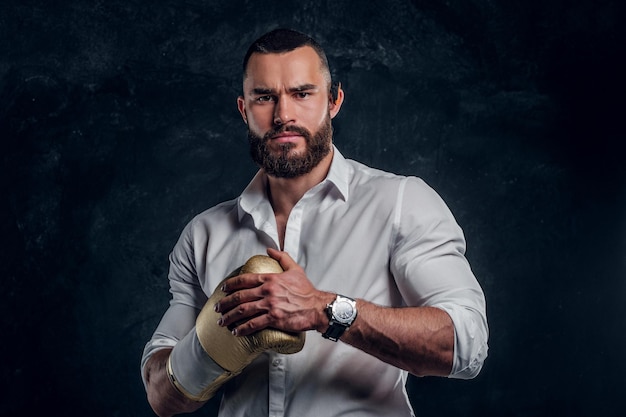 Angry serious man in white shirt is ready to fight while posing for photographer on the dark background.