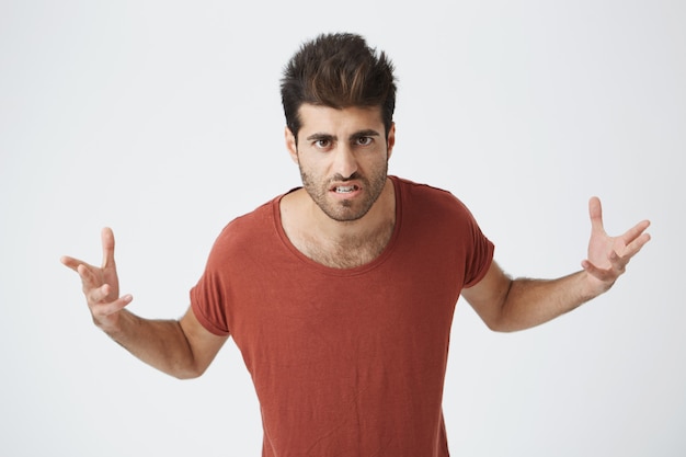 Angry spanish man in red shirt holding hands,  with irritated expression getting ready to fight with man on the street. Body language