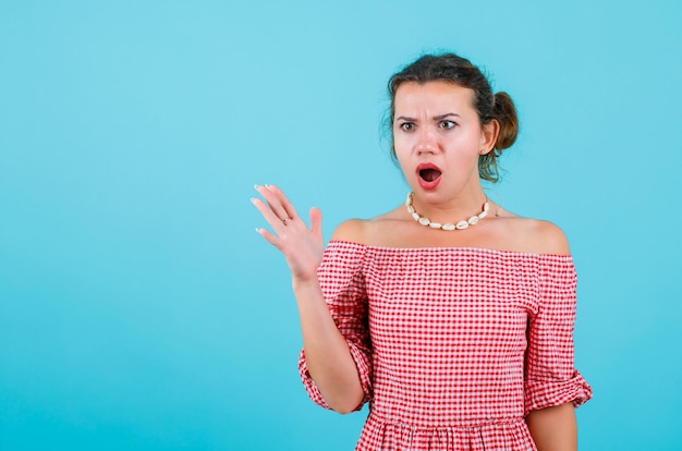 Foto gratuita la ragazza arrabbiata e sorpresa sta distogliendo lo sguardo alzando il rhand su sfondo blu