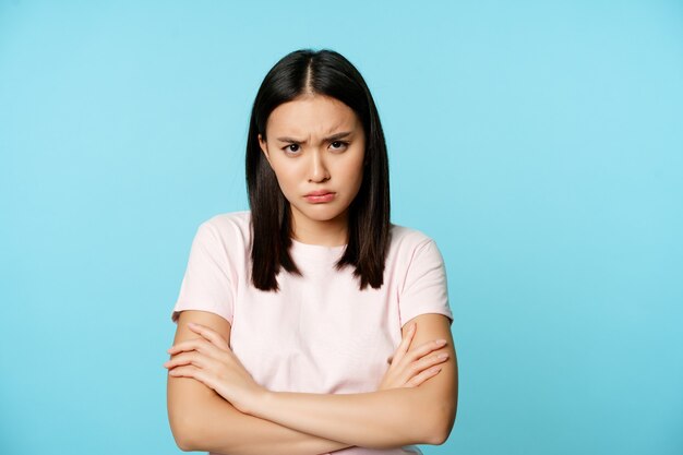 Angry teen asian girl standing in offended pose frowning and sulking feeling defensive standing disa...