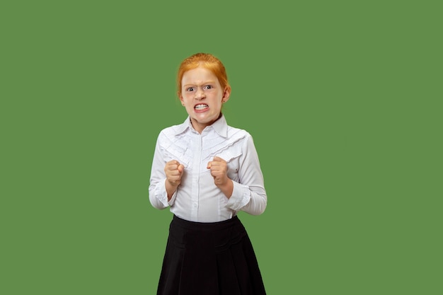 Angry teen girl standing on trendy green studio background. Female half-length portrait. Human emotions, facial expression concept. Front view.