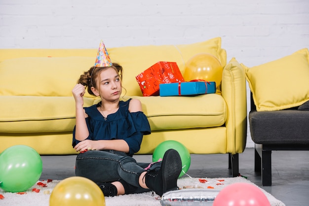 An angry teenage girl sitting on the white carpet with balloons at home