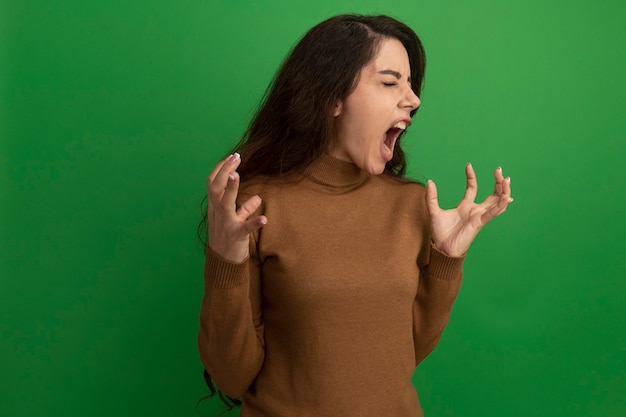 Angry with closed eyes young beautiful girl spreading hands isolated on green wall