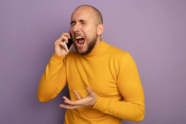 Angry with closed eyes young handsome guy speaks on phone isolated on purple wall