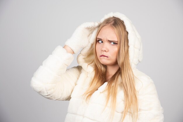 Angry woman in fur coat standing on gray wall.