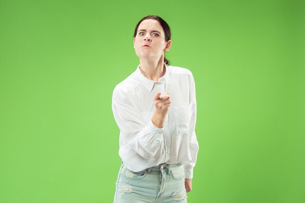 Сердитая женщина, смотрящая на камеру. Агрессивное положение женщины дела изолированное на предпосылке модной зеленой студии.