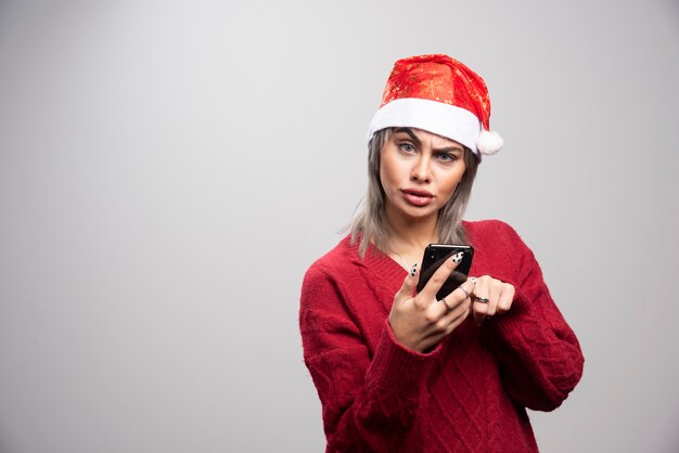 携帯電話を保持し、カメラを見ている赤いセーターの怒っている女性。