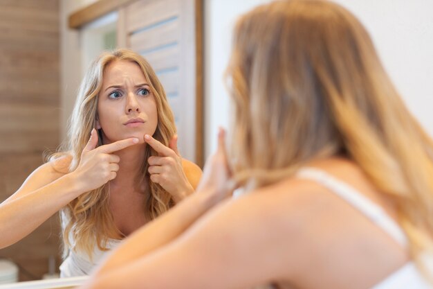 Angry woman squeezing  pimple from face