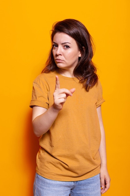 Angry woman with serious face pointing finger at camera in studio. Displeased person feeling upset and irritated doing gesture of frustration and rage, standing over isolated background.