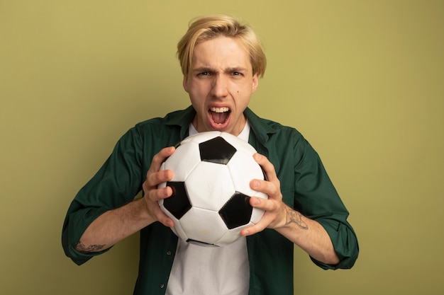 Free photo angry young blonde guy wearing green t-shirt holding ball