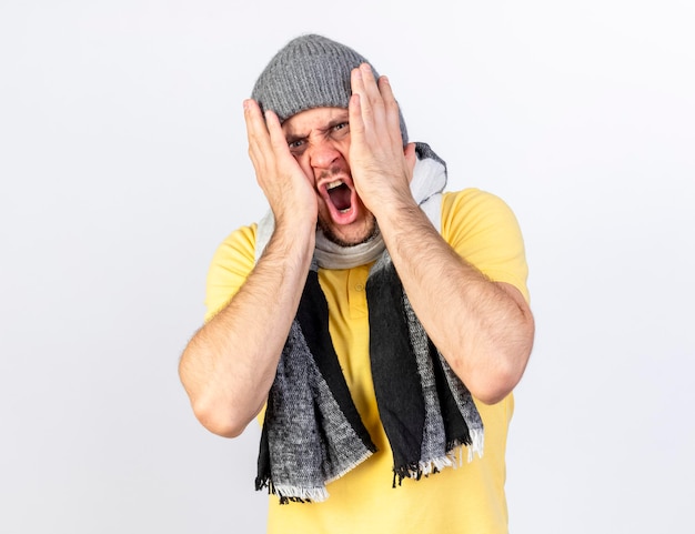 Angry young blonde ill slavic man wearing winter hat and scarf