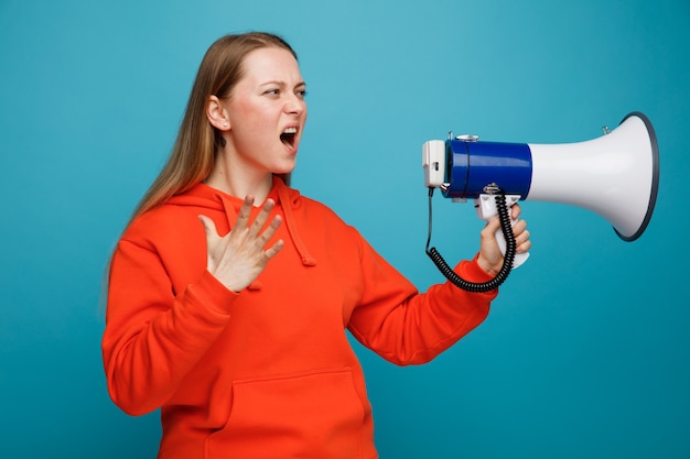 Angry young blonde woman holding speaker looking at side keeping hand in air shouting 