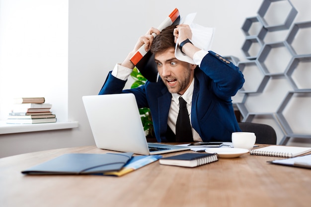 Free photo angry young businessman looking at laptop, office background.