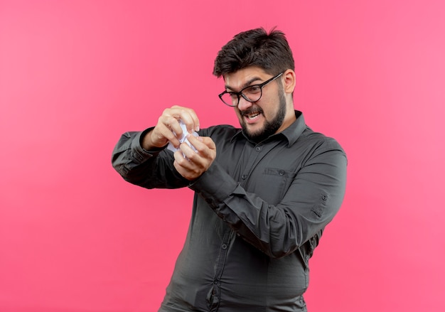 Free photo angry young businessman wearing glasses crushing paper isolated on pink background