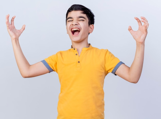 Сердитый молодой кавказский мальчик держит руки в воздухе с закрытыми глазами, изолированными на белом фоне