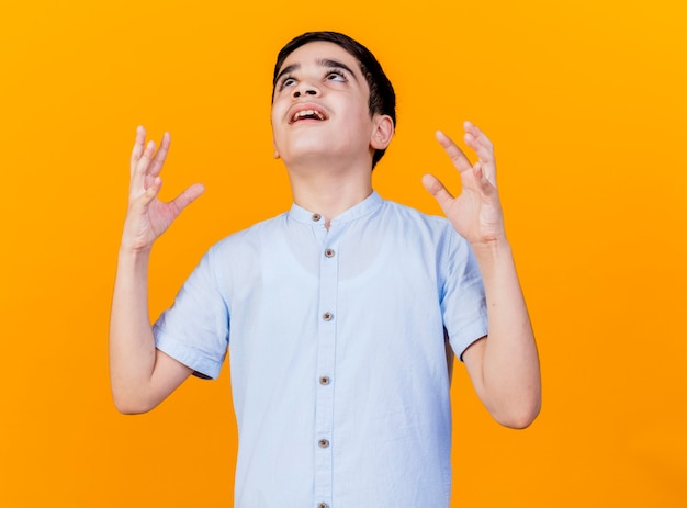 Free photo angry young caucasian boy looking up keeping hands in air isolated on orange background