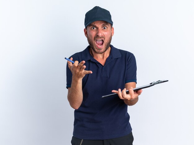 Angry young caucasian delivery man in blue uniform and cap holding clipboard and pen 