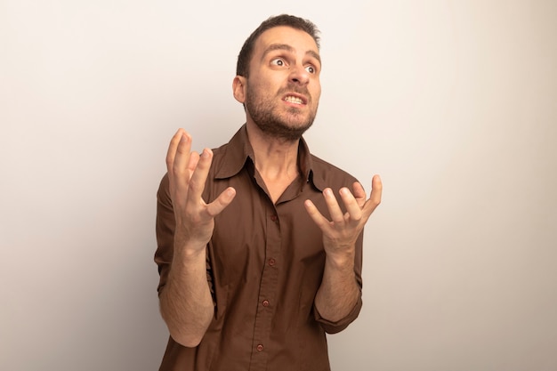 Angry young caucasian man keeping hands in air looking at side isolated on white background with copy space