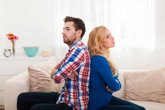 Free photo angry young couple sitting back to back at home