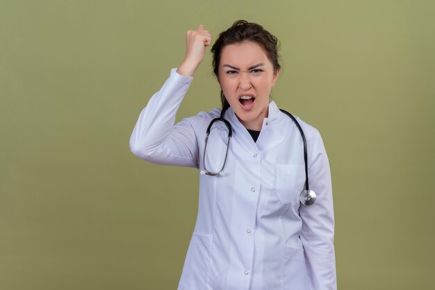 Сердитый молодой врач в медицинском халате со стетоскопом поднял кулак на зеленой стене