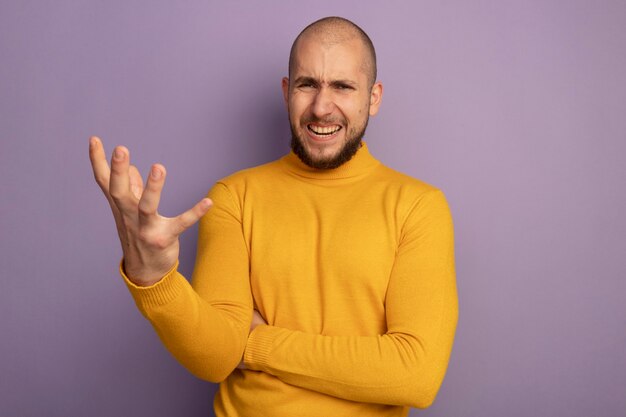 Angry  young handsome guy holding out hand  isolated on purple wall with copy space