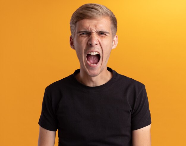 Angry young handsome guy wearing black shirt isolated on yellow wall