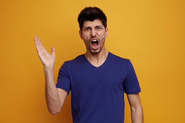 Angry young handsome man looking at camera showing empty hand on yellow background