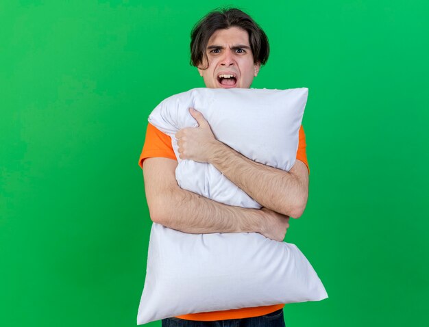 Angry young ill man hugged pillow isolated on green background