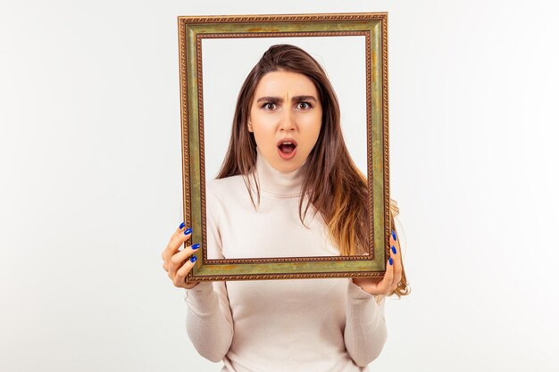 Angry young lady holding frame and looking through it