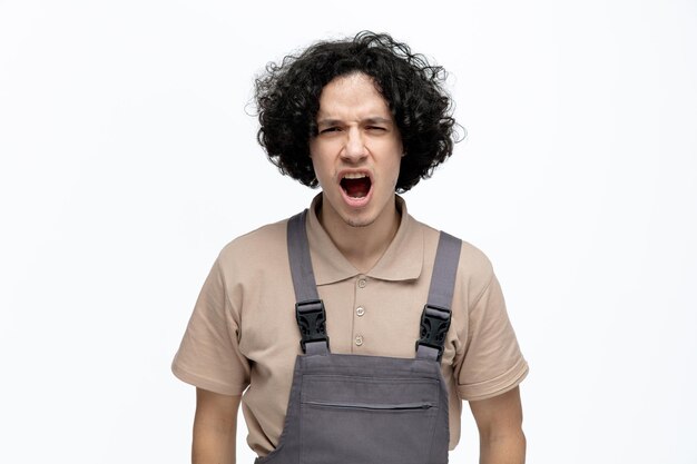 Angry young male construction worker wearing uniform looking at camera shouting isolated on white background