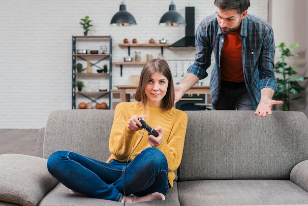 Un giovane arrabbiato guardando sorridente donna che gioca il videogioco in cucina