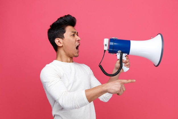 Angry young man standing in profile view looking and pointing at side shouting in loud speaker 