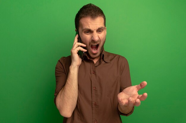緑の壁に隔離された空の手を示して見下ろして電話で話している怒っている若い男