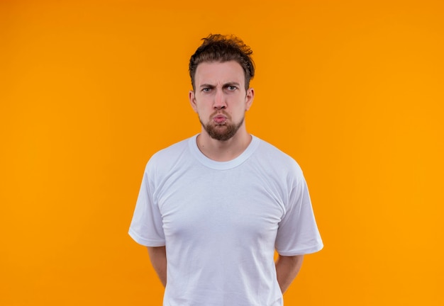 Сердитый молодой человек в белой футболке положил руку на изолированную оранжевую стену