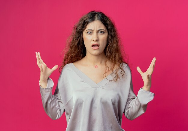 Angry young pretty girl spreads hands isolated on pink background