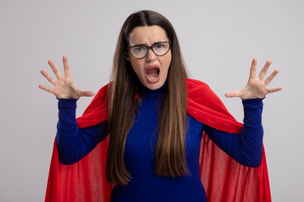 Angry young superhero girl wearing glasses raising hands isolated on white