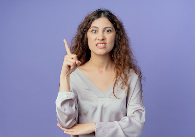 angry young woman points at side isolated on blue with copy space