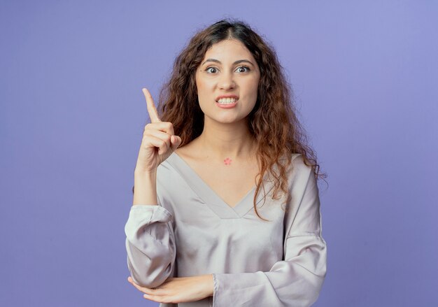 angry young woman points at side isolated on blue with copy space