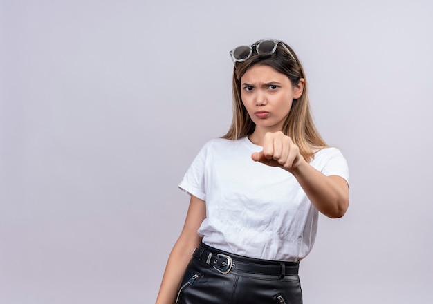 くいしばられた握りこぶしを見せながら笑っているサングラスの白いTシャツの怒っている若い女性