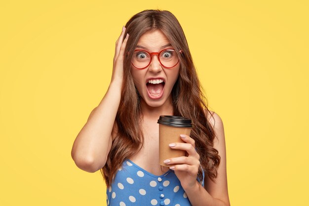 angry young woman with glasses posing against the yellow wall