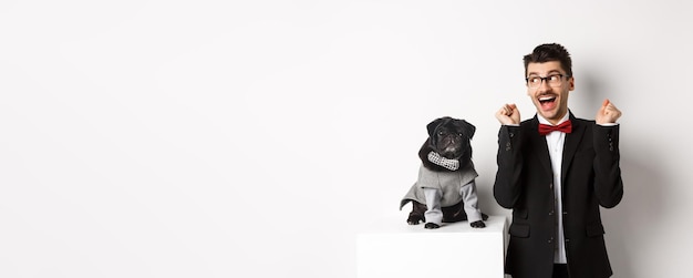 Free photo animals party and celebration concept cheerful dog owner in suit standing near cute black pug in cos