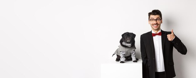 Animals party and celebration concept handsome young man in suit and cute black pug in costume stari