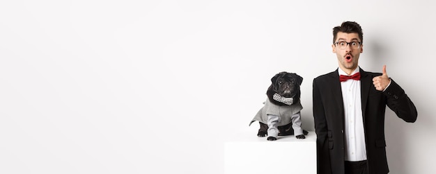 Free photo animals party and celebration concept handsome young man in suit and cute black pug in costume stari