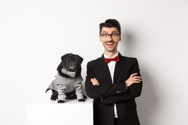 Animals, party and celebration concept. Happy dog owner in suit and puppy in costume looking excited at camera, having fun, standing over white background