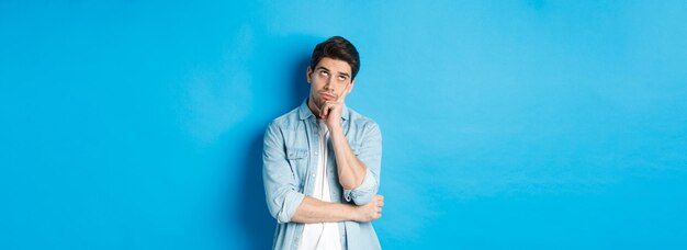 Annoyed adult man rolling eyes and looking bored standing indifferent against blue background in cas