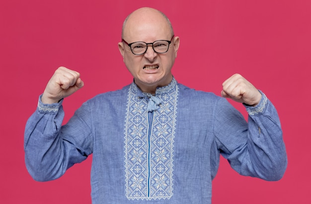 Free photo annoyed adult slavic man in blue shirt wearing glasses keeping fists