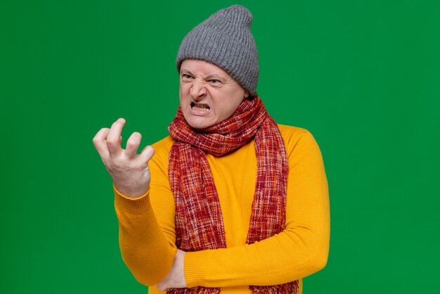 Annoyed adult slavic man with winter hat and scarf around his neck squeezing and looking at his fingers 