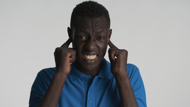 Annoyed African American man emotionally covering ears with fingers and does not want to hear anything isolated on white background So loud expression